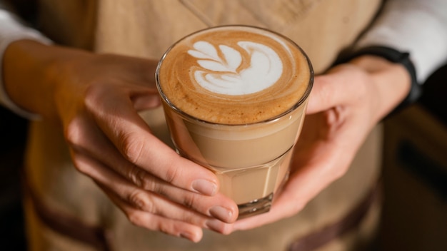 Barista femenina con delantal sosteniendo un vaso de café decorado