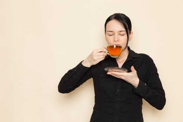 Barista femenina en pantalones de camisa negra con café marrón té seco equipo ingredientes haciendo y bebiendo té en la pared blanca