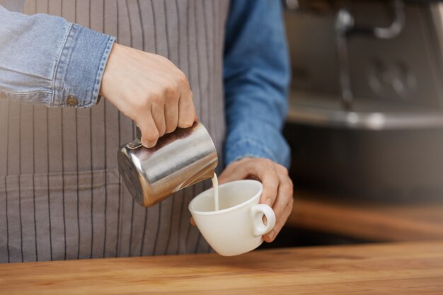 Barista haciendo una taza de café con leche, vertiendo leche en la taza.