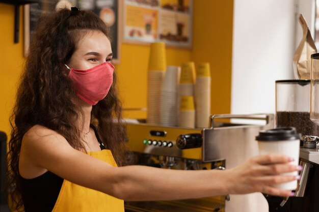 Barista con una máscara médica mientras da una taza de café