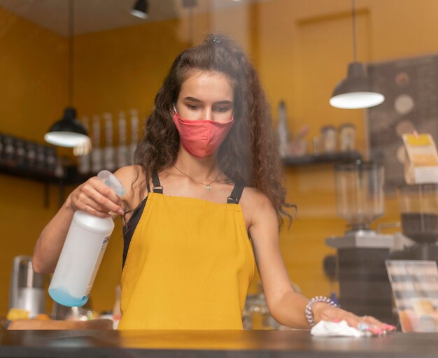 Barista con una máscara médica mientras limpia en la cafetería.