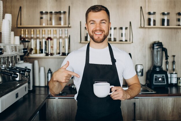 Barista masculino en la cafetería sosteniendo la taza por el mostrador