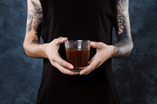 Barista masculino que se sostiene de cristal con café sobre gris.