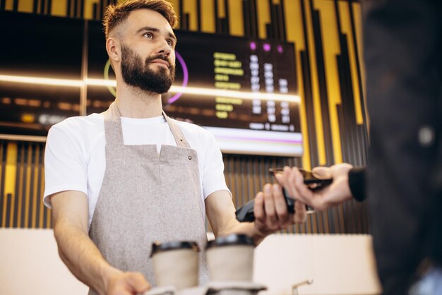 Barista masculino sosteniendo terminal mientras el cliente paga con tarjeta