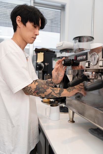 Barista masculino con tatuajes con la máquina de café en la cafetería.