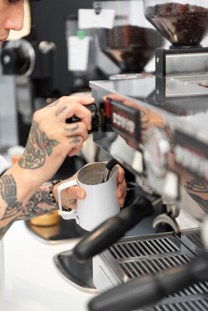 Barista masculino con tatuajes con la máquina de café en la cafetería.