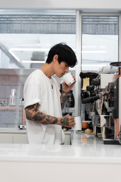 Barista masculino con tatuajes que huelen café recién molido en la taza