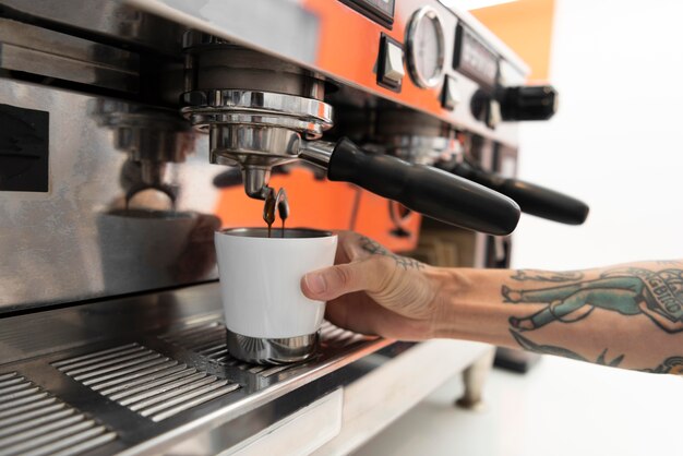 Barista masculino con tatuajes en el trabajo con la máquina de café