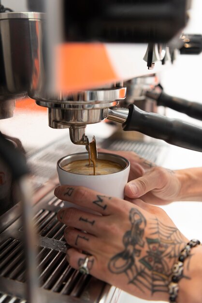 Barista masculino con tatuajes en el trabajo con la máquina de café