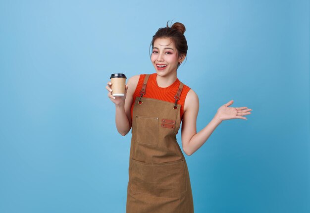 Barista mujer asiática que sirve al cliente sosteniendo una taza de café en una cafetería aislada sobre un fondo azul