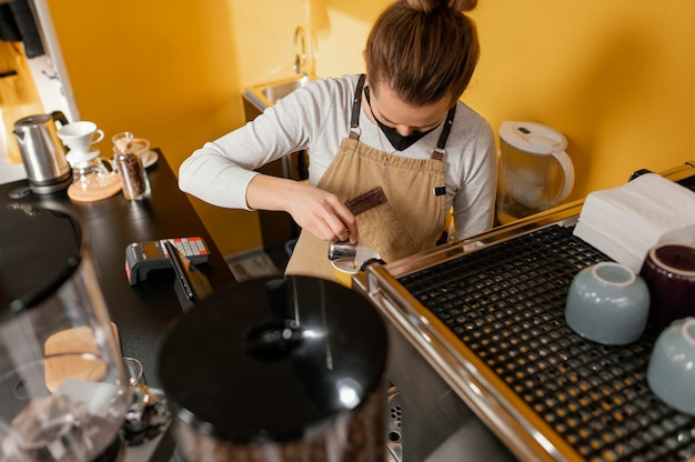 Barista mujer con máscara trabajando en la cafetería.