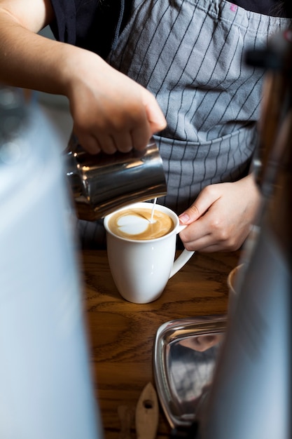 Barista profesional vertiendo espuma con leche en un café en la cafetería