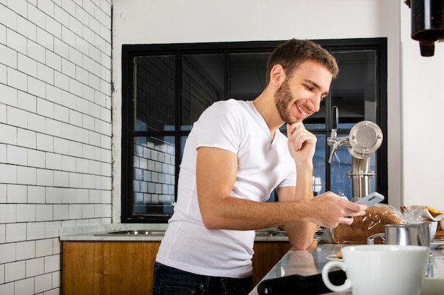 Barista sonriendo al teléfono inteligente detrás del mostrador en la cafetería.