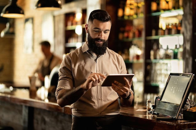 Barista sonriente usando tableta digital mientras trabaja en un bar