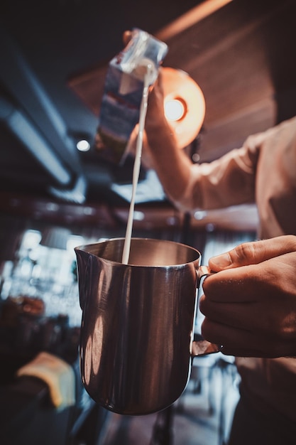 El barista talentoso está vertiendo leche en la jarra para café con leche o capuchino en su café.