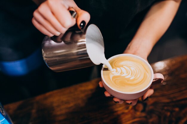 Barista vertiendo leche en el café en una cafetería.