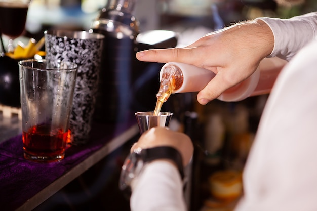 Barman en camisa blanca vertiendo bebida increíble para cóctel