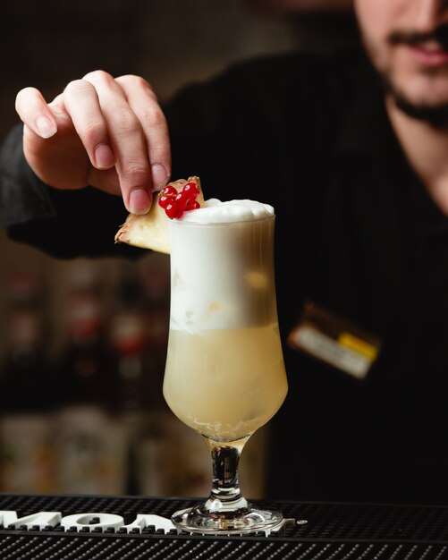 Un barman decorando jugo de piña con bayas y rodaja de piña.