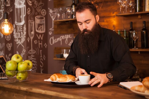 Barman guapo detrás de una barra con un café preparado. Pub de época.