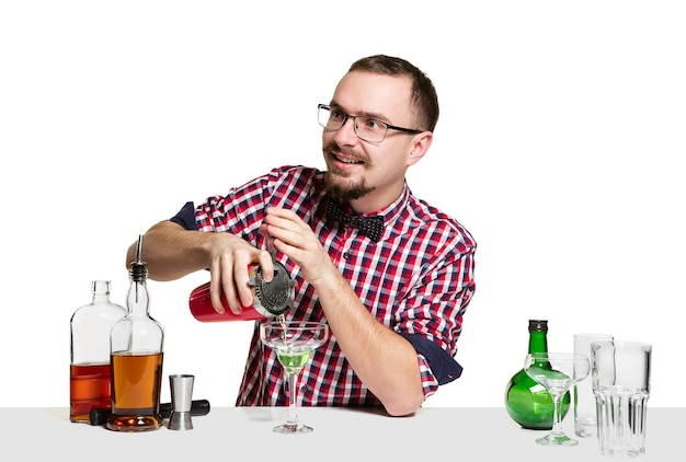 El barman masculino experto está haciendo cócteles en aislados en la pared blanca.