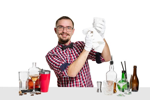 Barman masculino experto está haciendo cócteles en el estudio aislado en la pared blanca