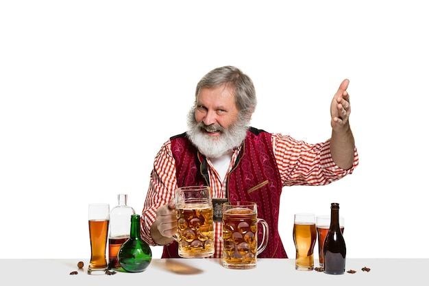 El barman masculino experto senior con cerveza en el estudio aislado en la pared blanca