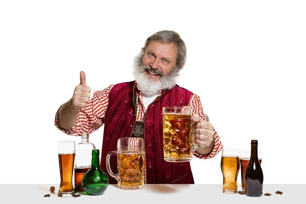 El barman masculino experto senior con cerveza en el estudio aislado en la pared blanca
