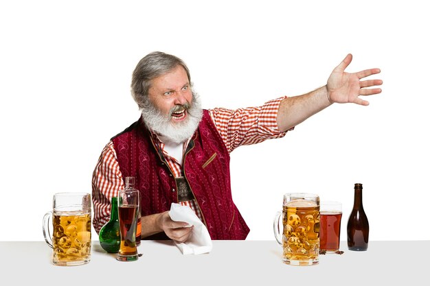 El barman masculino experto senior con cerveza en el estudio aislado en la pared blanca