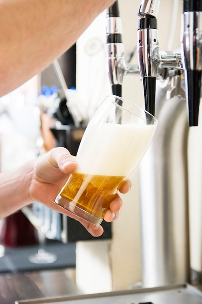 Barman que vierte la cerveza fresca en pub
