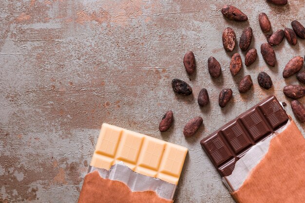 Barra de chocolate blanco y negro con granos de cacao crudos en el fondo rústico