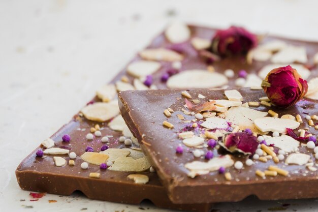 Barra de chocolate con frutas secas y rosa sobre fondo blanco