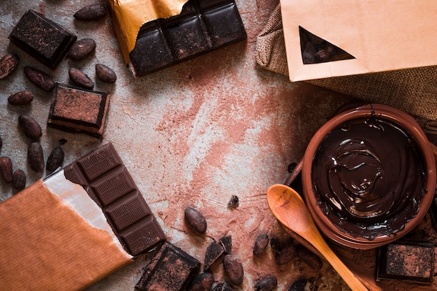 Barra de chocolate, granos de cacao y crema de chocolate en la mesa