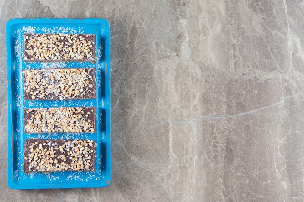 Barra de chocolate en rodajas con nueces sobre placa de madera sobre mármol.