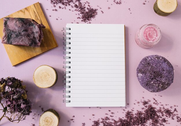 Barra de jabón de lavanda; tocón de madera; exfoliación corporal; Flor seca y bloc de notas de una sola página sobre fondo rosa.