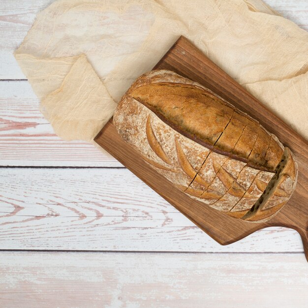 Barra de pan con las rebanadas en la tajadera y el mantel sobre el escritorio de madera