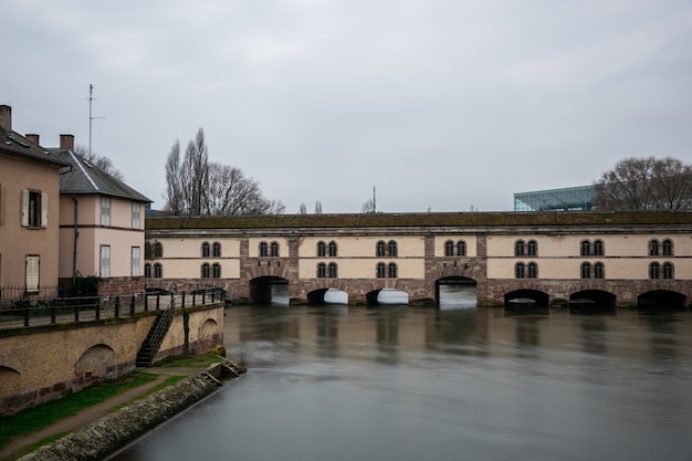 Barrage Vauban rodeado de agua y edificios bajo un cielo nublado en Estrasburgo en Francia