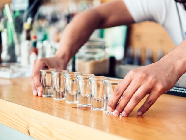 Bartender poner fila de vasos de chupito en mostrador