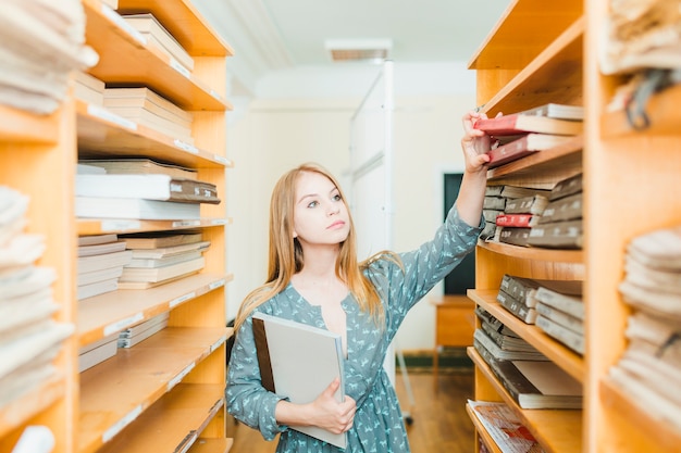 Bastante adolescente tomando libros de texto del estante