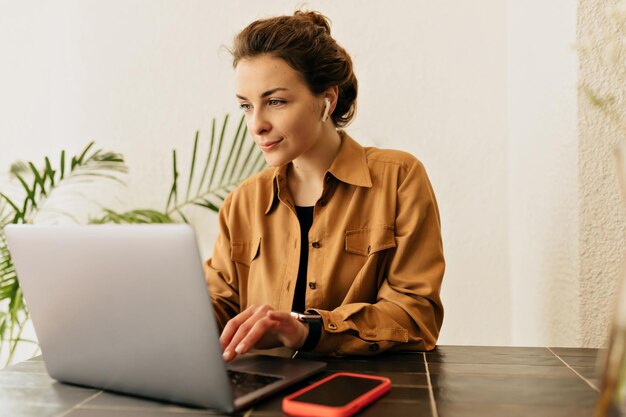 Bastante alegre mujer morena en auriculares está trabajando en la computadora portátil en la mesa cosas de trabajo envolvente Estado de ánimo alegre tomando un descanso trabajando estudiando relajación verdadera emoción