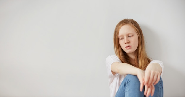 Bastante joven adolescente sentada en el suelo en casa desesperación triste solo