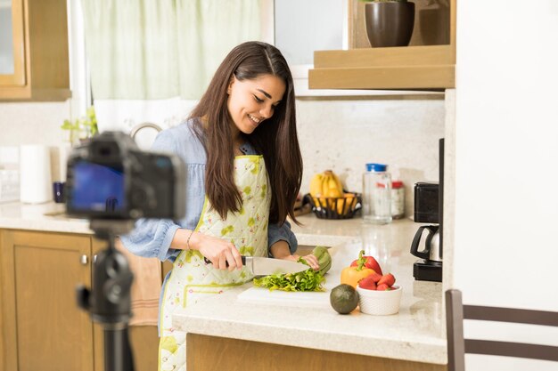 Bastante joven bloguera grabando un video y cocinando un plato para su vlog de comida