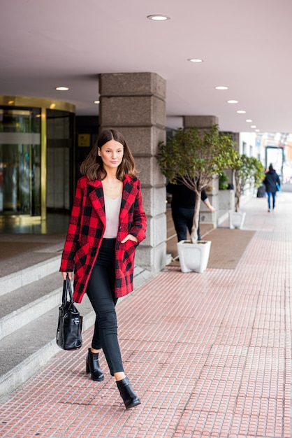 Bastante joven caminando saliendo de un hotel vistiendo ropa elegante otoño