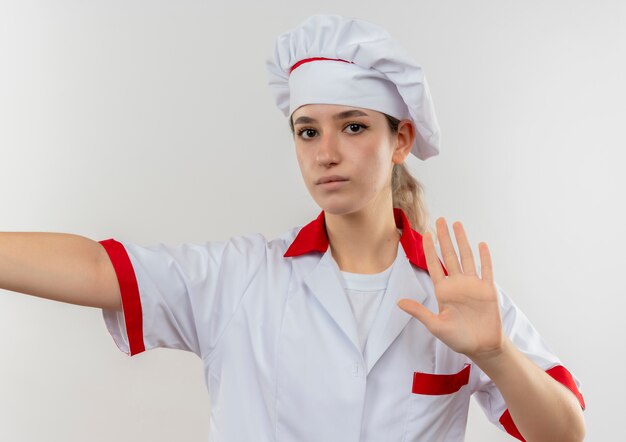 Bastante joven cocinero en uniforme de chef con el brazo abierto gesticulando no y mirando