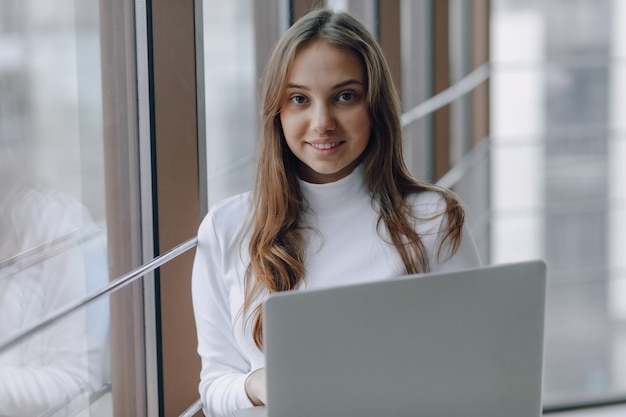 Bastante joven con una computadora portátil junto a la ventana