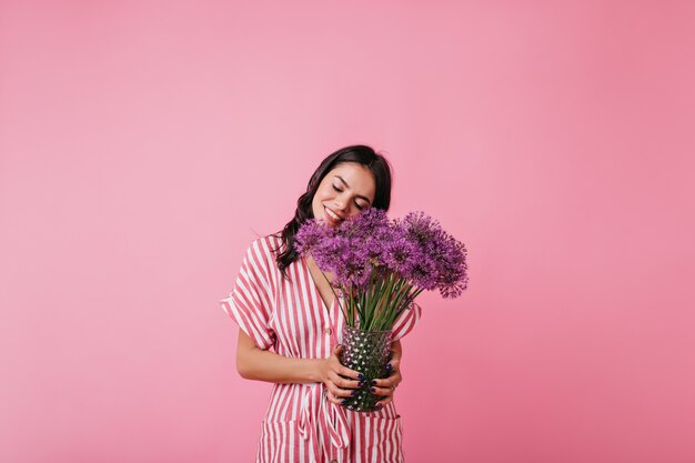 Bastante joven disfruta del aroma de las flores. Instantánea de modelo rizado en top rosa de moda.