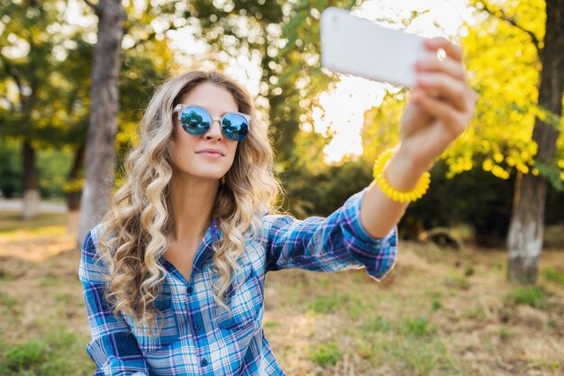 Bastante joven elegante atractiva mujer rubia sonriente sentada en el parque, estilo casual de verano