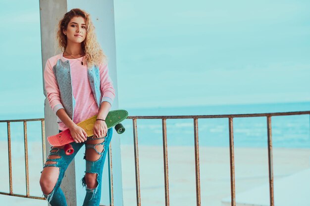 Bastante joven está posando para el fotógrafo con monopatín cerca de la playa.