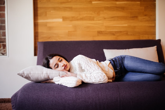 Bastante joven está tomando una siesta diaria entre el trabajo para hacer en el sofá oscuro en el apartamento de moda