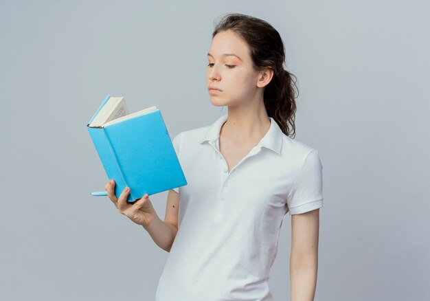 Bastante joven estudiante sosteniendo y leyendo un libro con lápiz en mano aislado sobre fondo blanco con espacio de copia