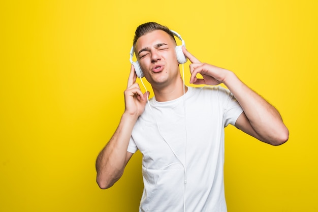 Bastante joven guapo en camiseta blanca escuchar música con sus nuevos auriculares aislados en la pared amarilla